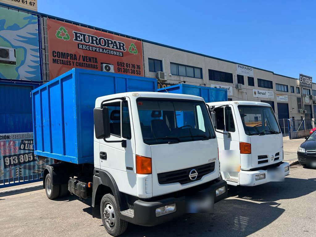 Dos camiones blancos con caja azul aparcados junto a la nave