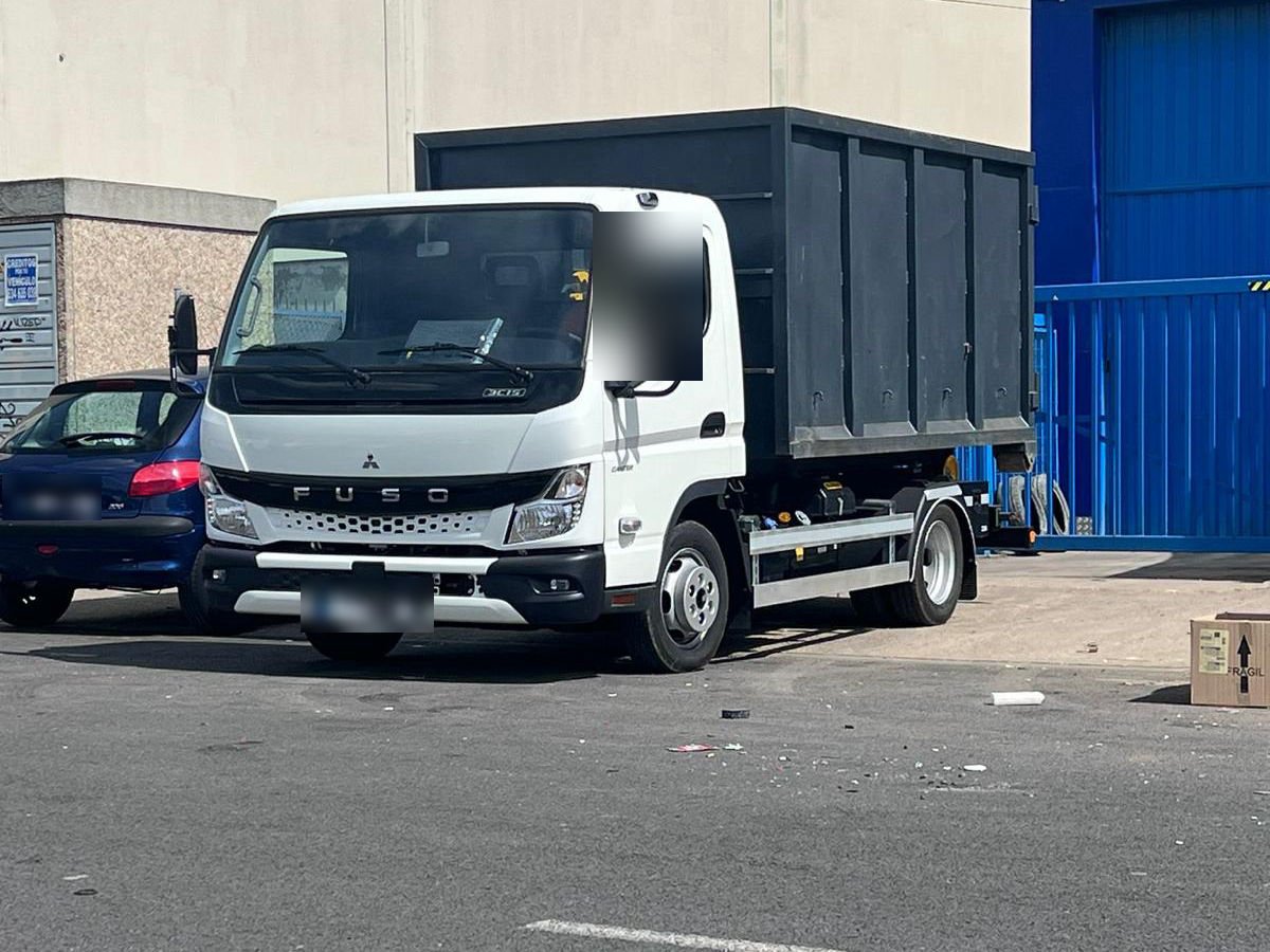 Camión blanco con un contenedor negro cargado, aparcado en el polígono